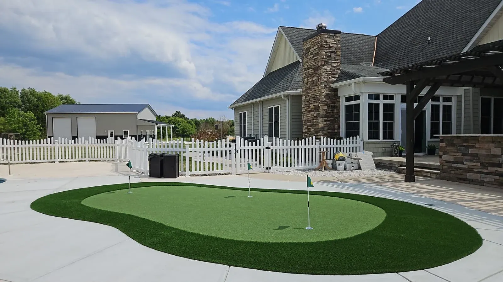 Three-hole artificial turf putting green with a turf fringe, set into a pool deck beside a stone patio