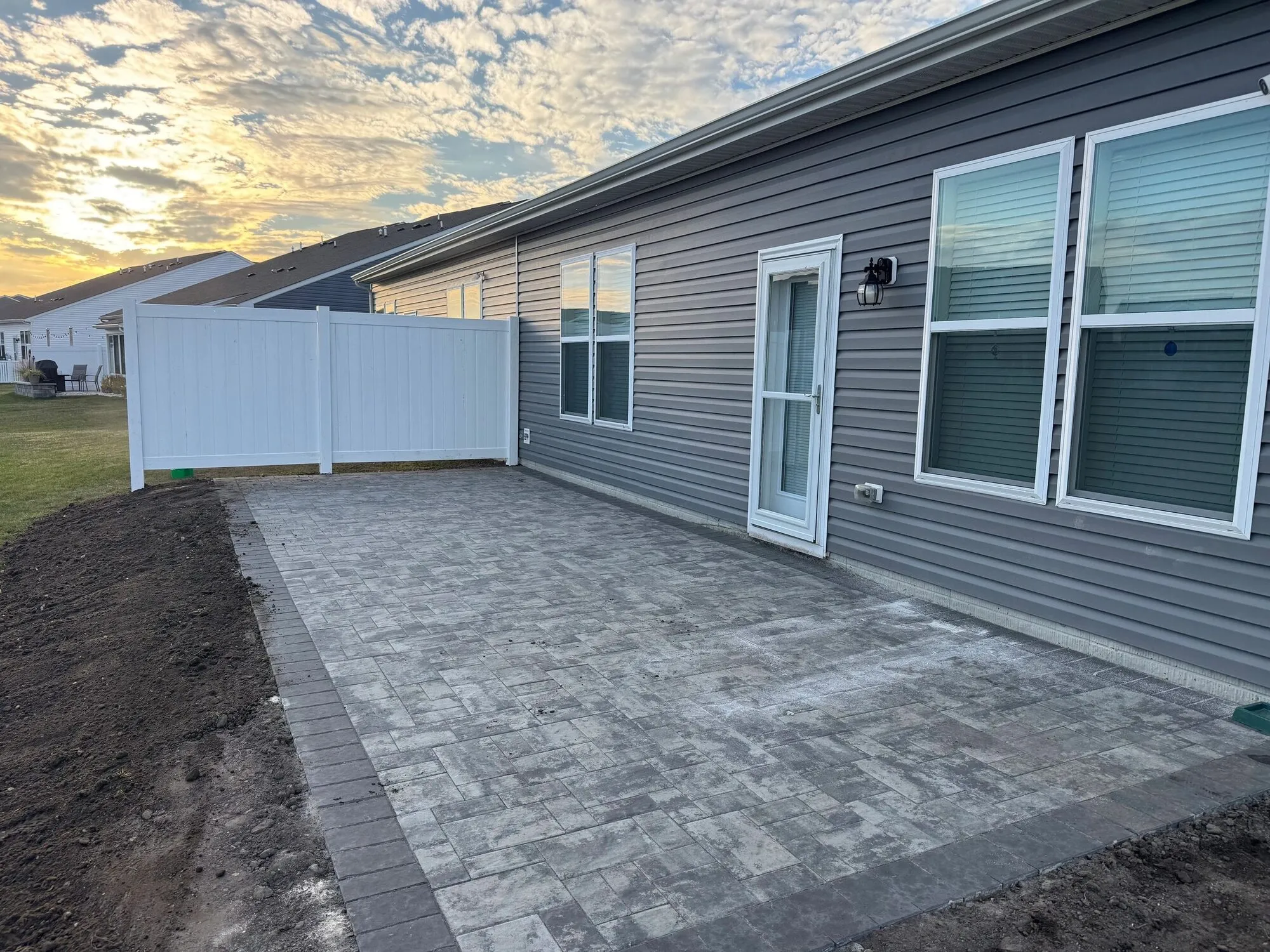 New gray paver patio with a contrasting border along the back of a house